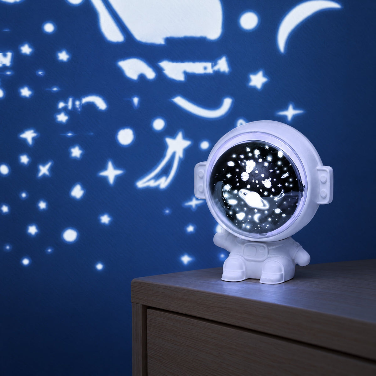 White astronaut projector on a nightstand projecting planets, stars and rockets onto a dark blue wall