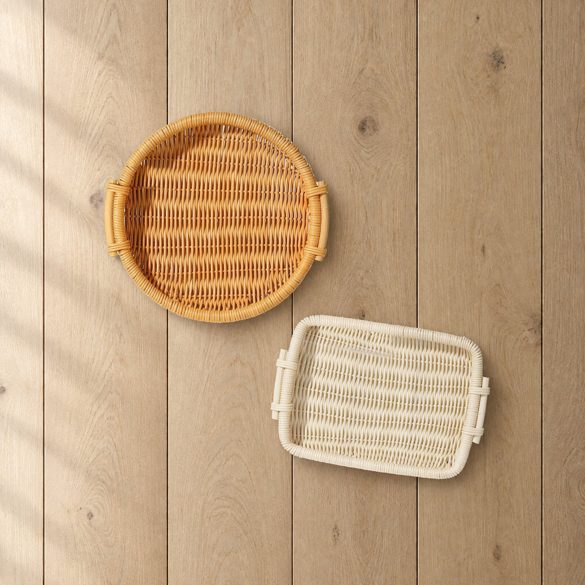 Round honey and rectangular natural rattan trays on a light oak table, seen from above