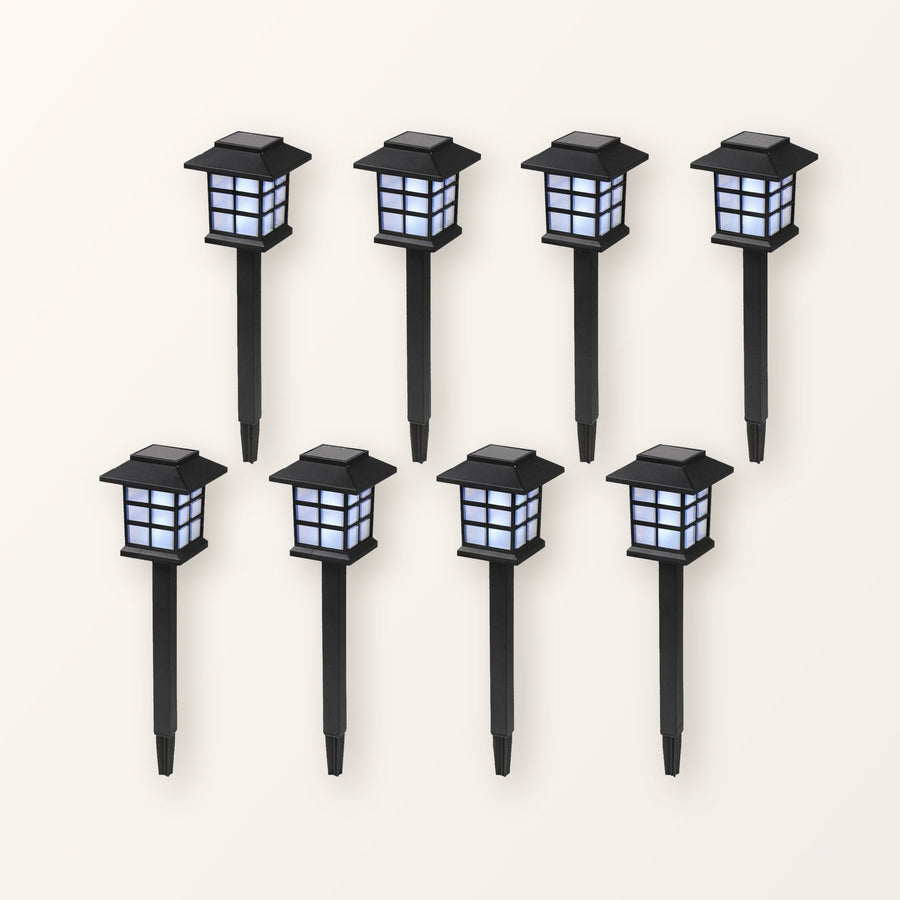 Eight black pagoda-style solar path lanterns on ground stakes, in two rows on a plain cream background