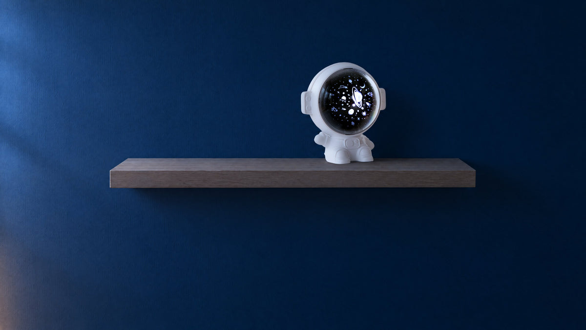 White astronaut star projector with its visor lit, on a light oak shelf against an indigo wall at dusk