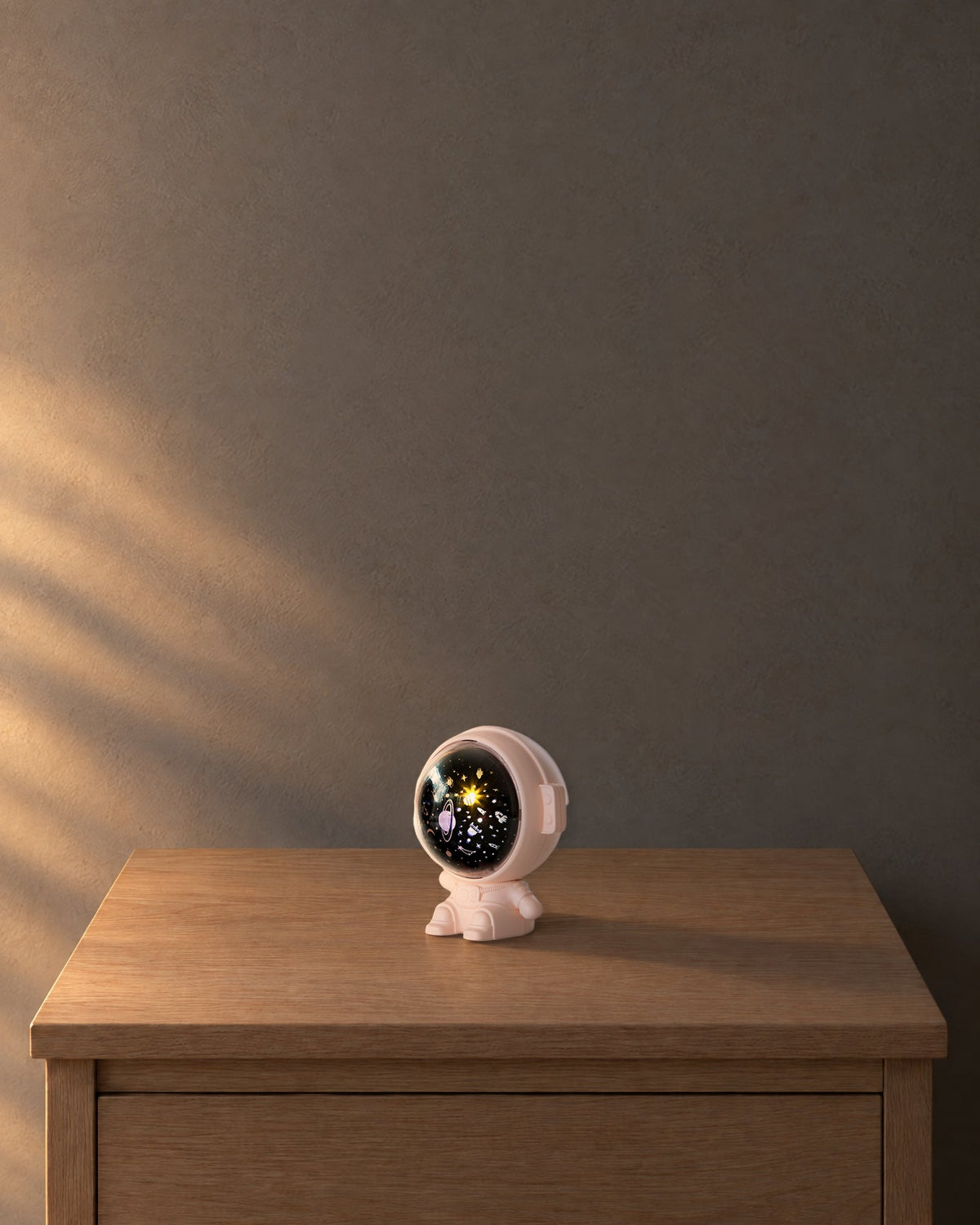 Pink astronaut projector, 4.8 in tall, visor lit, on an oak bedside table at dusk, drawn to scale