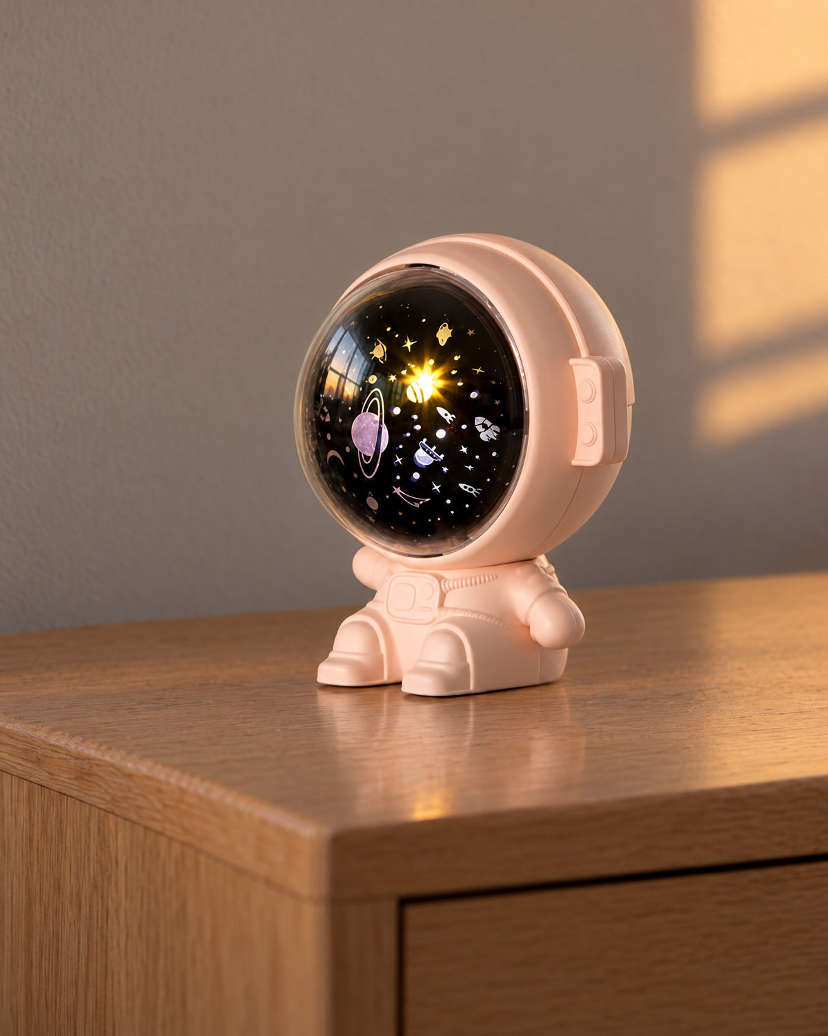 Pink astronaut star projector with its visor lit, on an oak bedside table at dusk