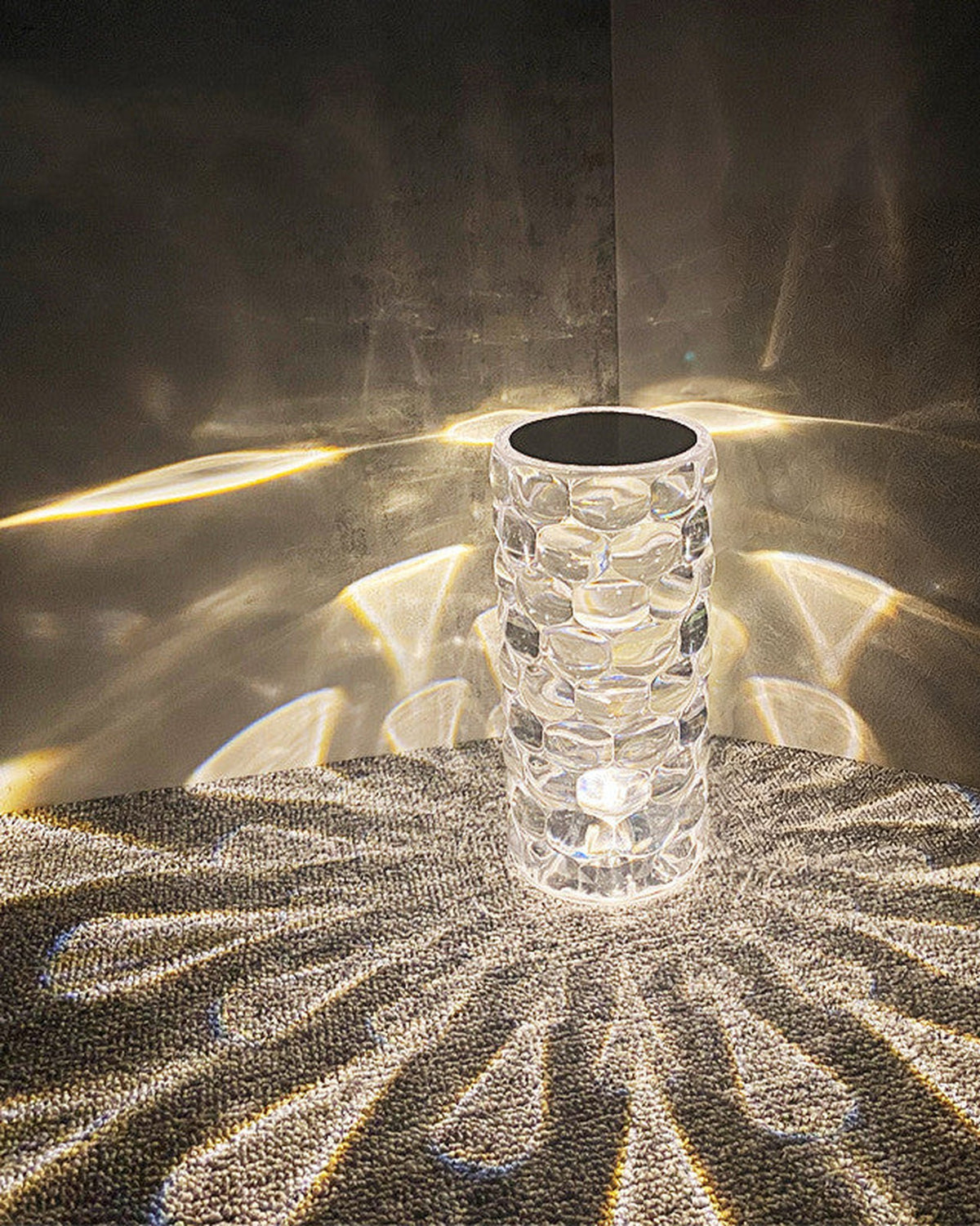 Crystal-look lamp in a warm white tone at night, throwing droplet shapes across a grey surface and the wall