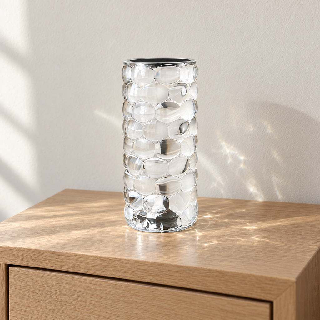 Crystal-look acrylic lamp switched off in daylight on an oak nightstand, clear bubble facets and a silver rim