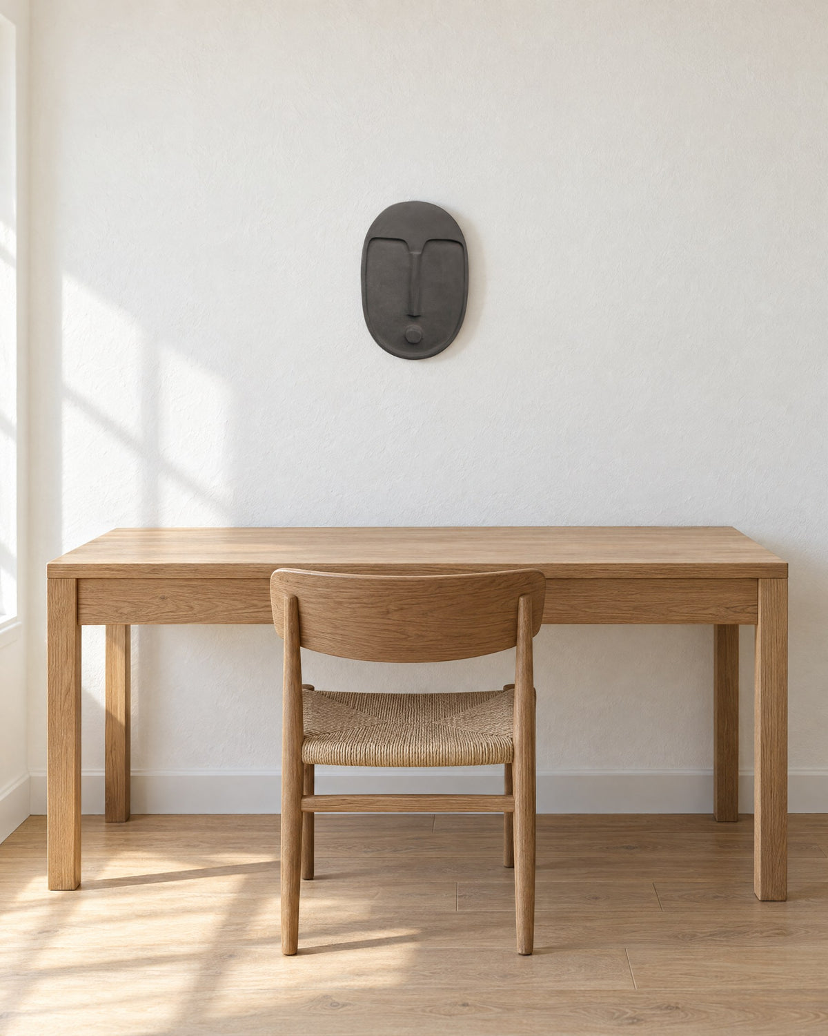 Anthracite grey ceramic wall mask on a white wall above a plain oak desk and chair