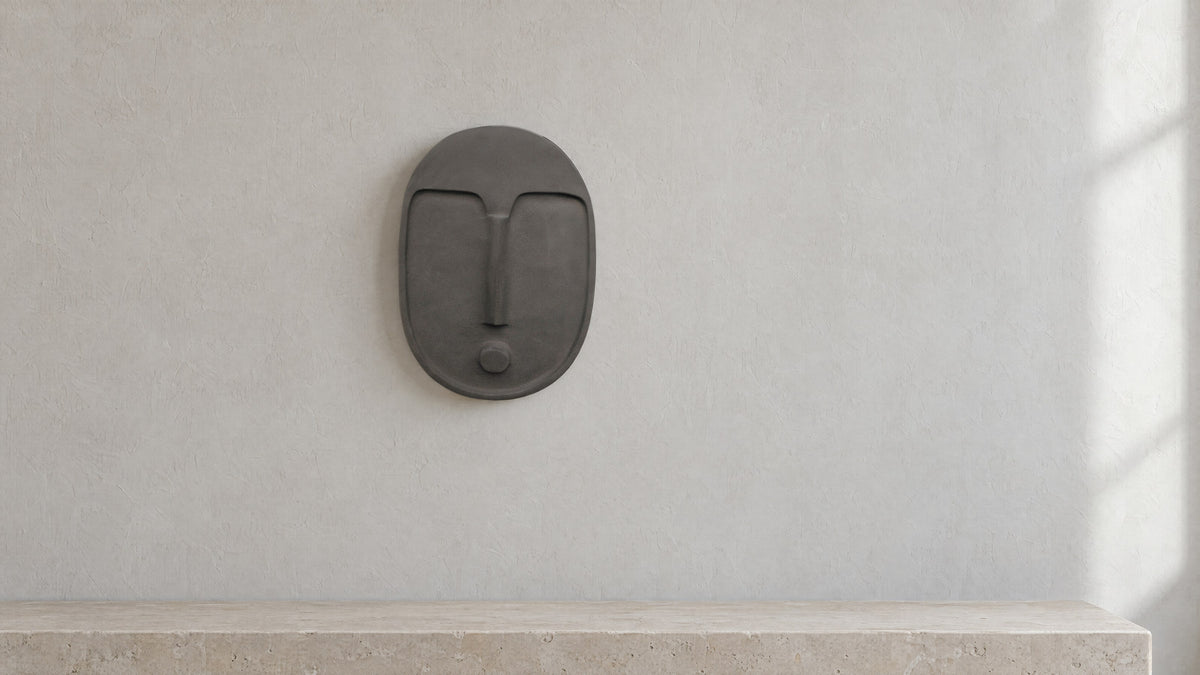 Anthracite grey ceramic wall mask on a pale grey limewash wall above a plain limestone bench, in soft daylight