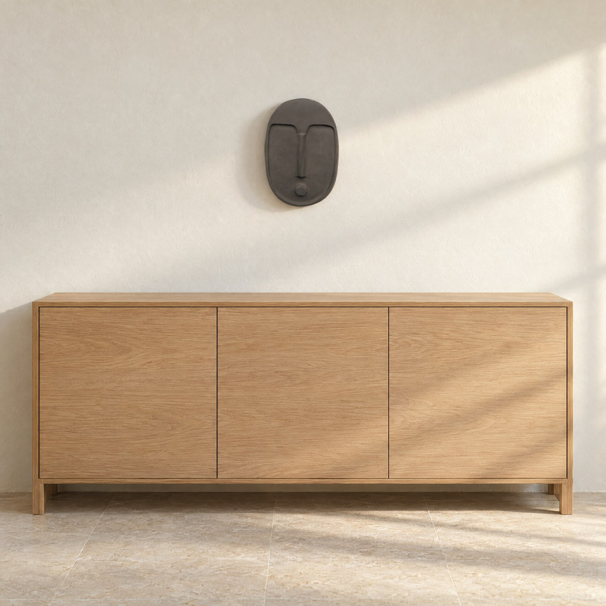 Anthracite grey ceramic wall mask on a warm white wall above a light oak sideboard