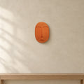 Terracotta orange ceramic wall mask hung on a warm plaster wall above an oak console