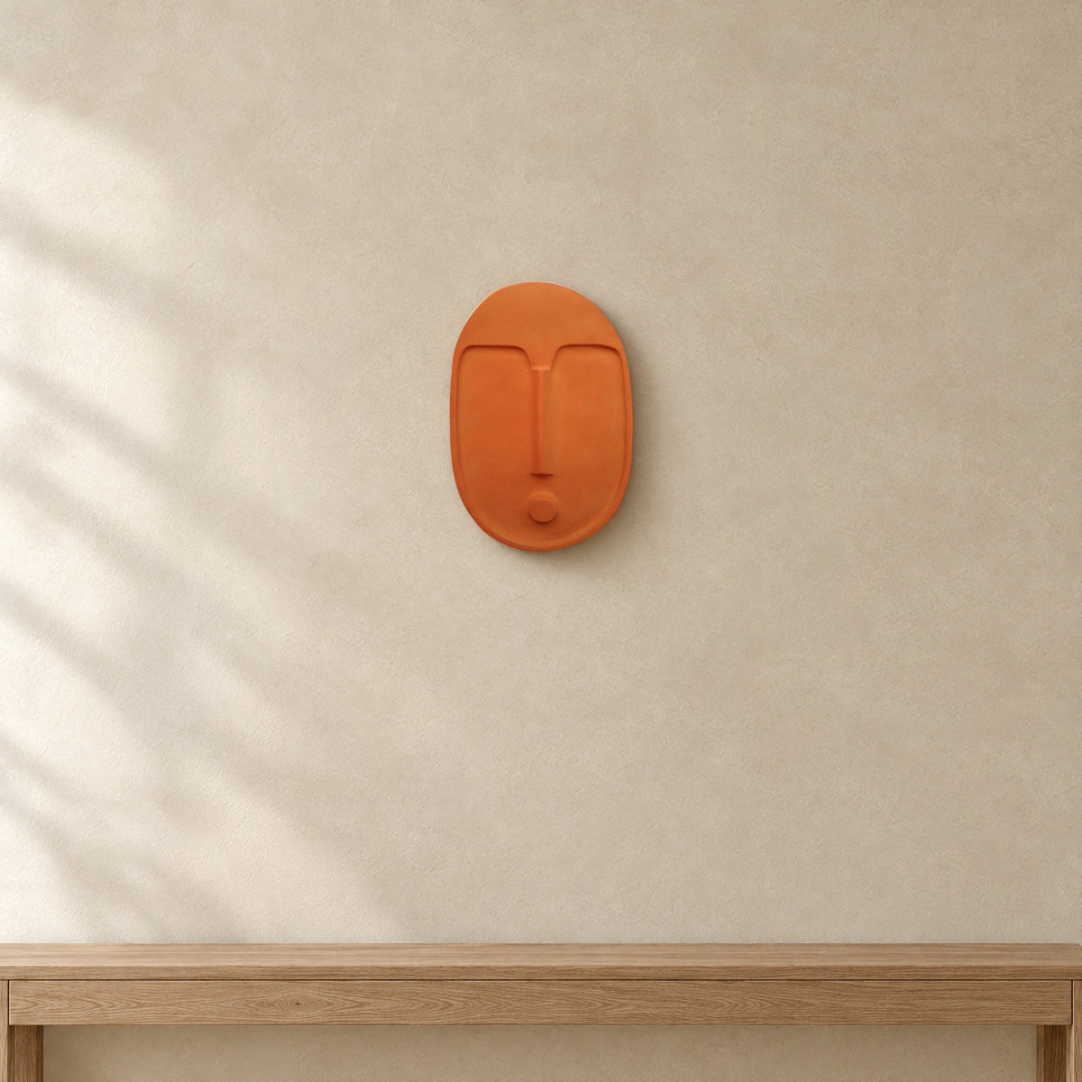 Terracotta orange ceramic wall mask hung on a warm plaster wall above an oak console