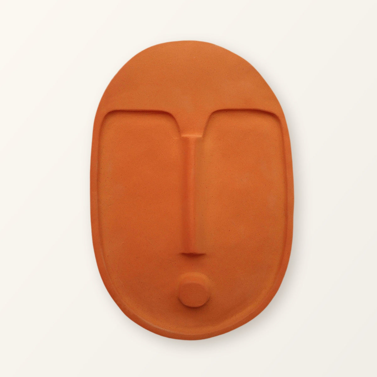 Terracotta orange ceramic wall mask, front view on a warm off-white background
