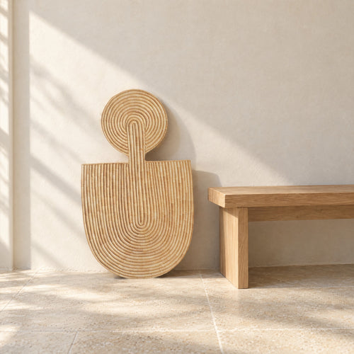 Abstract Wall Mask 1 leaning against a pale limewash wall beside a low oak bench, in morning sun