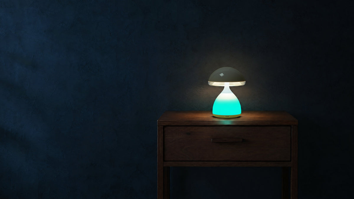 Mushroom table lamp switched on at night, white light under its cap and a teal glow in its base, on a walnut nightstand