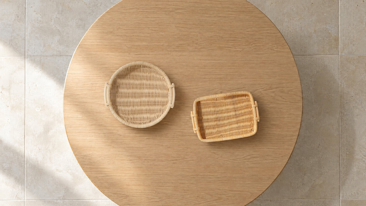 Round natural and rectangular honey woven rattan trays, empty, on a round oak table seen from above