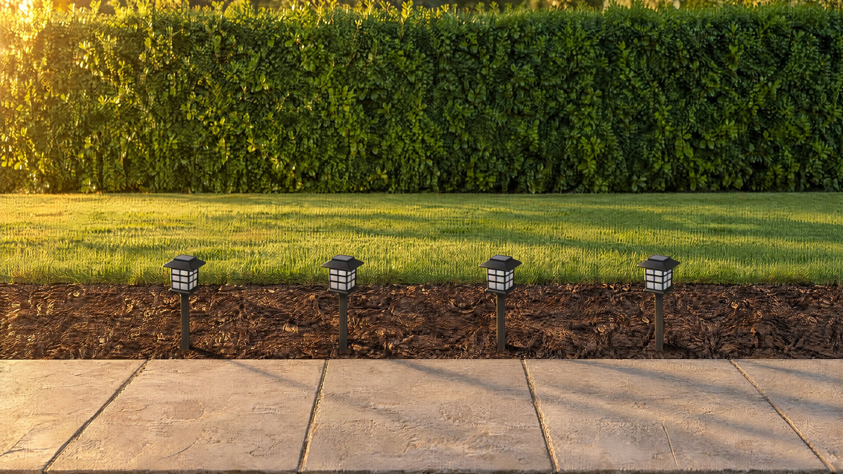 Four black pagoda solar path lanterns, switched off, in a bark mulch border beside a stone path in late sun