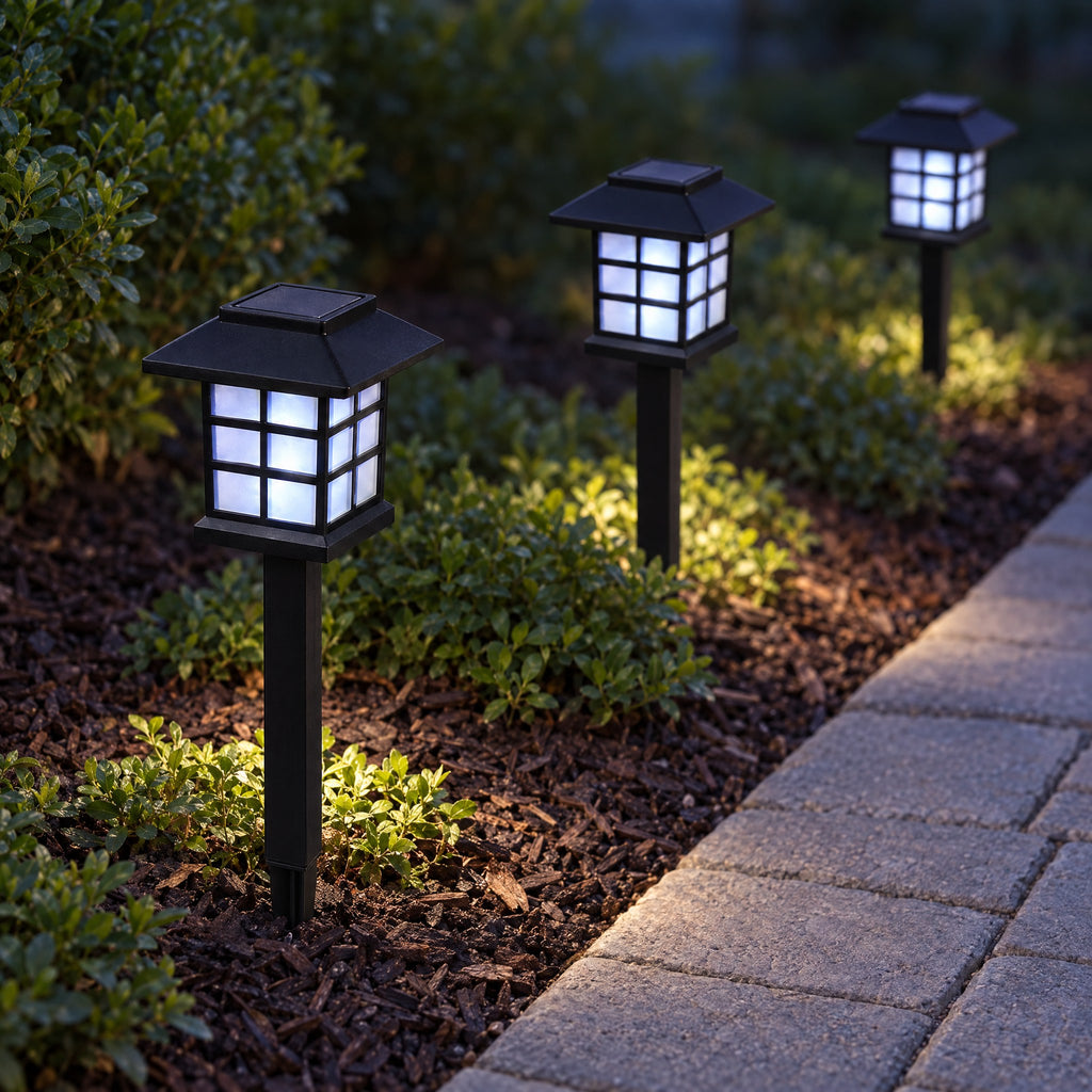 Three pagoda solar path lanterns glowing cool white at dusk in a mulch border beside a stone path