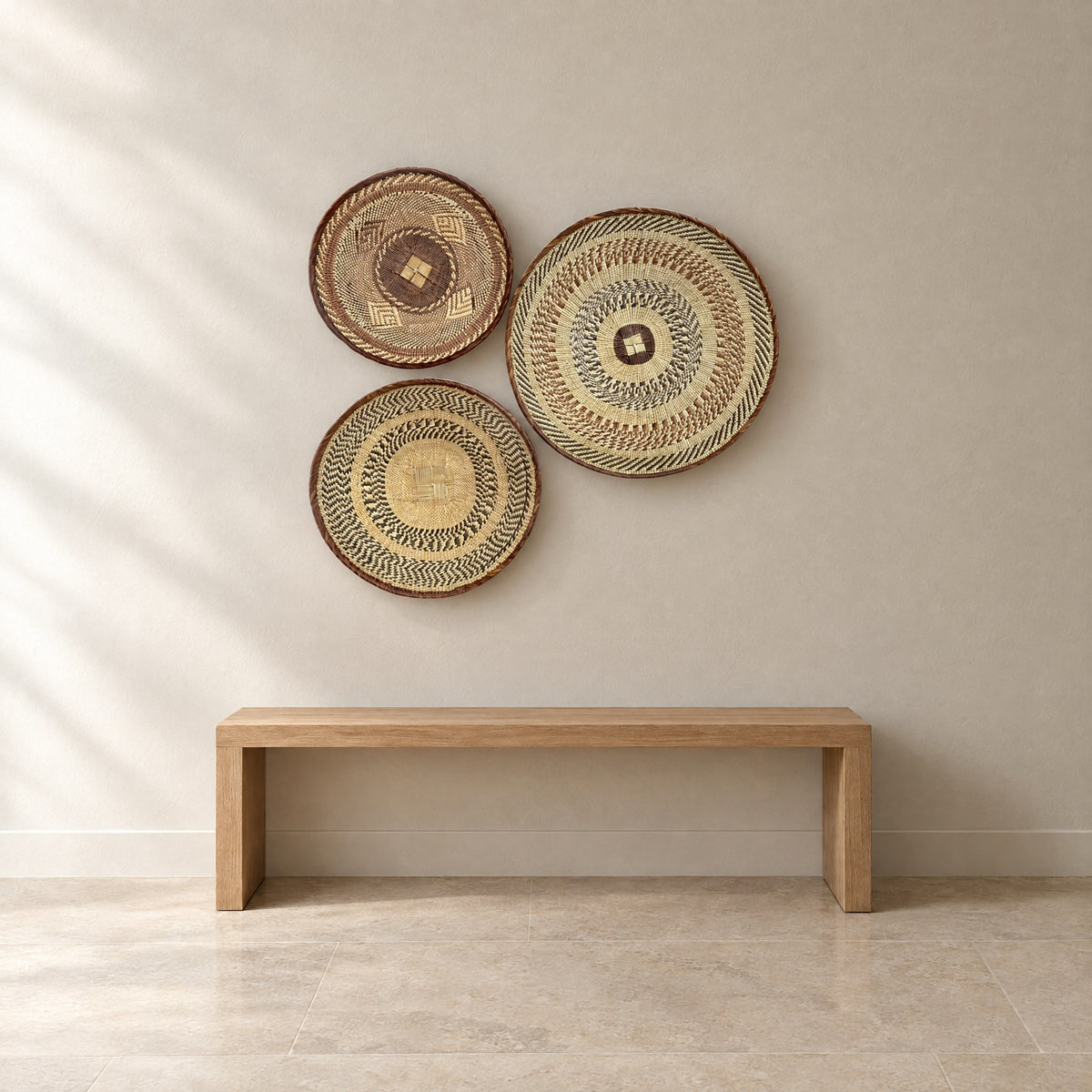 Set of three handwoven Tonga baskets hung on a plaster wall above an oak bench